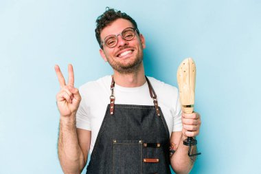 Kafkasyalı genç kunduracı mavi arka planda izole edilmiş neşeli ve tasasız parmakları olan bir barış sembolü gösteriyor..