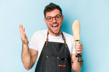 Kafkasyalı genç kunduracı mavi arka planda izole edilmiş. Hoş bir sürpriz alıyor, heyecanlı ve el kaldırıyor..