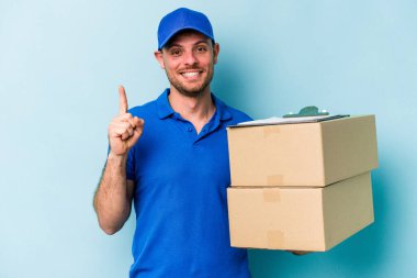 Beyaz tenli genç teslimatçı mavi arka planda bir numarayı parmağıyla gösteriyor..