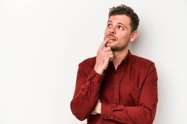 Beyaz arka planda izole edilmiş genç beyaz bir adam şüpheli ve şüpheci bir ifadeyle yana bakıyor..