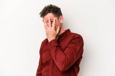 Beyaz arka planda izole edilmiş genç beyaz bir adam kameraya parmaklarıyla göz kırpıyor, yüzünü kapatmaktan utanıyor..