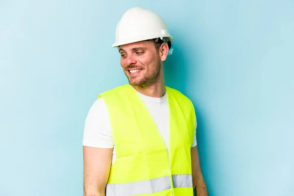 Young Laborer Caucasian Man Isolated Blue Background Looks Aside Smiling — 스톡 사진