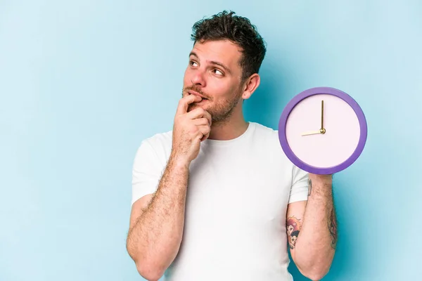 Young Caucasian Man Holding Clock Isolated Blue Background Relaxed Thinking — Stockfoto