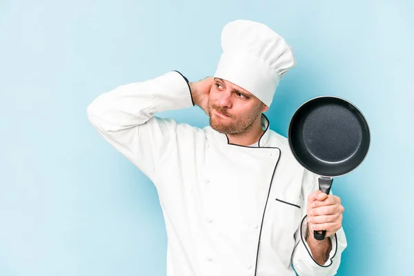 年轻的高加索厨师拿着一只被蓝色背景隔离的飞盘 背对着头 思考着 做出选择 — 图库照片