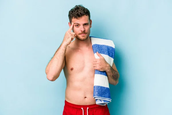 Young Caucasian Man Holding Beach Towel Isolated Blue Background Pointing — Φωτογραφία Αρχείου