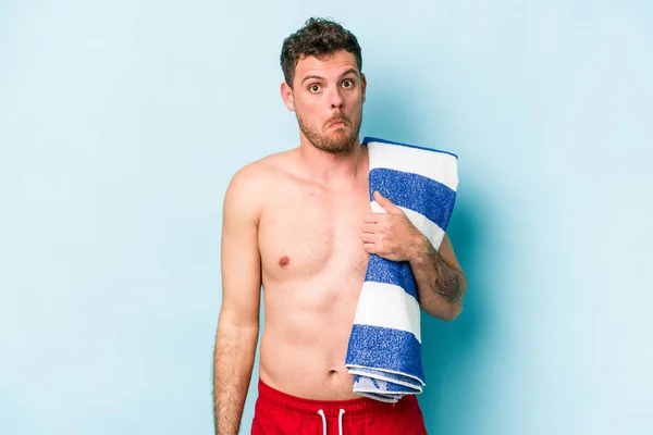 Young Caucasian Man Holding Beach Towel Isolated Blue Background Shrugs — Photo