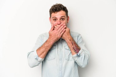 Beyaz arka planda izole edilmiş genç beyaz adam elleriyle ağzını kapatırken şok oldu..