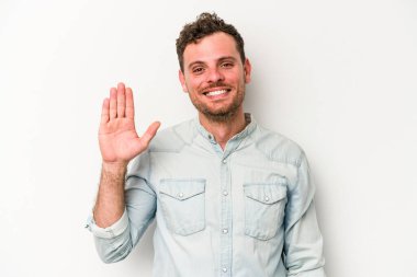 Beyaz arka planda izole edilmiş genç beyaz bir adam gülümseyerek beş numarayı parmaklarıyla gösteriyor..