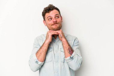 Beyaz arka planda izole genç beyaz adam ellerini çenesinin altında tutuyor, mutlu bir şekilde yana bakıyor..