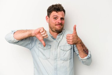 Beyaz arka planda izole edilmiş genç beyaz bir adam baş parmaklarını aşağı ve yukarı kaldırıyor, zor seçim konsepti