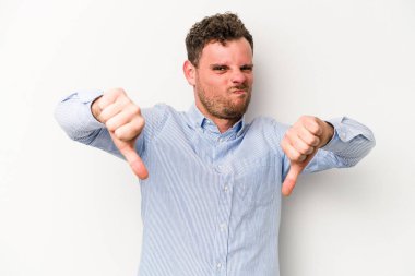 Beyaz arka planda izole edilmiş genç beyaz bir adam baş parmağını aşağı gösteriyor ve hoşlanmadığını ifade ediyor..
