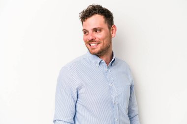 Beyaz arka planda izole edilmiş genç beyaz adam gülümseyen, neşeli ve keyifli bir tarafa bakıyor..