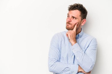 Beyaz arka planda izole edilmiş genç beyaz bir adam şüpheli ve şüpheci bir ifadeyle yana bakıyor..