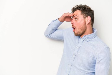 Beyaz arka planda izole edilmiş genç beyaz bir adam uzaklara bakıyor ve elini alnına koyuyor..