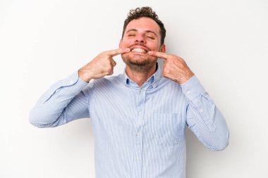 Beyaz arka planda izole edilmiş genç beyaz adam gülümsüyor, parmaklarını ağıza doğrultuyor..