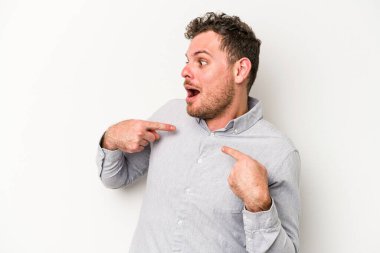 Beyaz arka planda izole edilmiş genç beyaz bir adam parmağını göstererek şaşırdı, geniş bir gülümsemeyle..