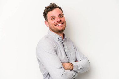 Beyaz arka planda kendini güvende hisseden, kararlılıkla kollarını kavuşturan beyaz tenli genç bir adam..