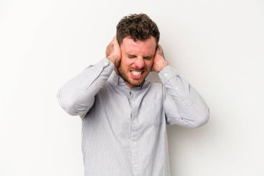 Beyaz arka planda izole edilmiş genç beyaz bir adam kulaklarını elleriyle kapatıyor..