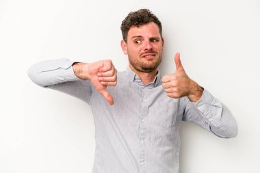 Beyaz arka planda izole edilmiş genç beyaz bir adam baş parmaklarını aşağı ve yukarı kaldırıyor, zor seçim konsepti