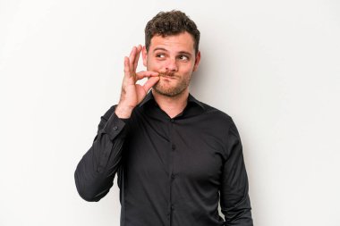 Beyaz arka planda izole edilmiş beyaz tenli genç bir adam parmakları dudaklarında bir sır saklıyor..