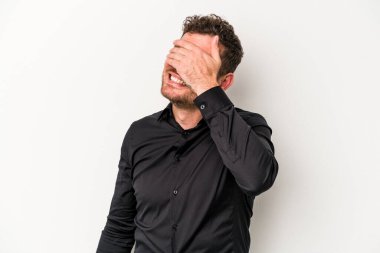 Beyaz arka planda soyutlanmış beyaz tenli genç bir adam elleriyle gözlerini kapatıyor, geniş bir gülümsemeyle bir sürpriz bekliyor..