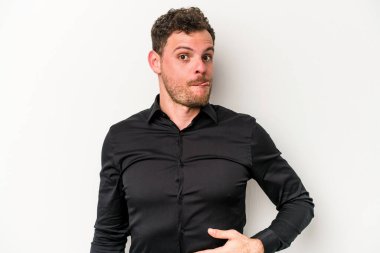 Beyaz arka planda izole edilmiş genç beyaz adam karnına dokunuyor, nazikçe gülümsüyor, yemek yiyor ve tatmin oluyor..