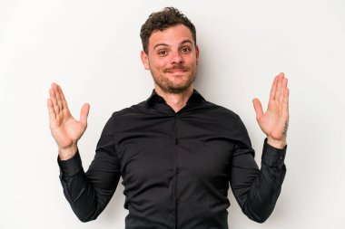 Beyaz arka planda izole edilmiş genç beyaz bir adam işaret parmaklarıyla küçük bir şey tutuyor, gülümsüyor ve kendinden emin..