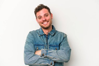 Beyaz arka planda kendini güvende hisseden, kararlılıkla kollarını kavuşturan beyaz tenli genç bir adam..