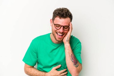 Beyaz arka planda izole genç beyaz adam mutlu bir şekilde gülüyor ve ellerini karnının üstünde tutarak eğleniyor..