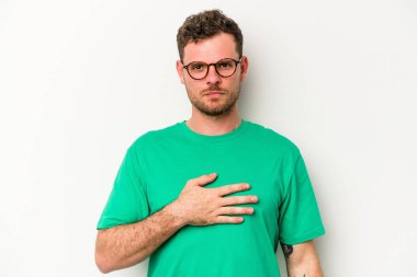 Beyaz arka planda izole edilmiş genç beyaz adam yemin ediyor, elini göğsüne koyuyor..