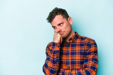 Mavi arka planda izole edilmiş, üzgün ve dalgın hisseden, kopyalama alanına bakan genç beyaz bir adam..