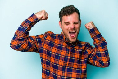 Mavi arka planda izole edilmiş genç beyaz bir adam zaferden sonra yumruğunu kaldırıyor, kazanan konsept..