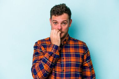 Mavi arka planda izole edilmiş, tırnak yiyen, gergin ve endişeli genç bir beyaz adam..