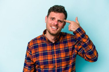 Mavi arka planda izole edilmiş genç beyaz adam işaret parmağıyla bir hayal kırıklığı jesti gösteriyor..