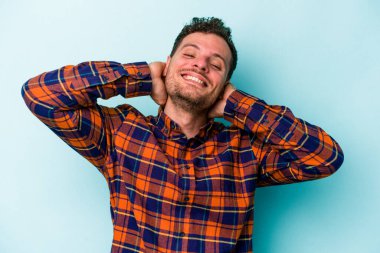 Mavi arka planda izole edilmiş genç beyaz adam kollarını uzatıyor, rahat bir konumda..