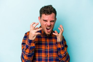 Mavi arka planda izole edilmiş genç beyaz adam gergin elleriyle çığlık atıyor..