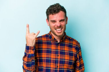 Mavi arka planda izole edilmiş genç beyaz adam boynuzlarını devrim konsepti olarak gösteriyor..