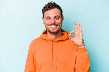 Kafkasyalı genç adam mavi arka planda izole edilmiş neşeli ve kendinden emin..