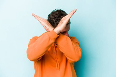 Kafkasyalı genç adam mavi arka planda izole edilmiş iki kolu çapraz tutuyor, inkar kavramı.