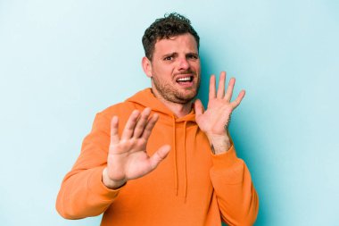 Mavi arka planda izole genç beyaz adam yakın bir tehlike nedeniyle şoka uğruyor