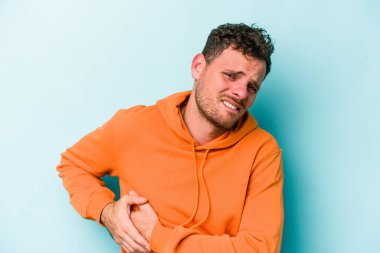 Mavi arka planda karaciğer ağrısı çeken, karnı ağrıyan genç beyaz bir adam..