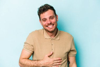 Mavi arka planda izole edilmiş genç beyaz adam karnına dokunuyor, nazikçe gülümsüyor, yemek yiyor ve tatmin oluyor..