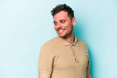 Mavi arka planda soyutlanmış genç beyaz bir adam gülümsüyor, neşeli ve keyifli görünüyor..