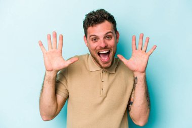 Mavi arka planda izole edilmiş genç beyaz adam hoş bir sürpriz alıyor, heyecanlı ve el kaldırıyor..