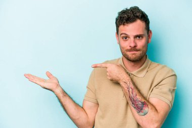 Kafkasyalı genç adam mavi arka planda izole edilmiş. Elinde palmiye ağacının bir kopyası olduğu için heyecanlı..