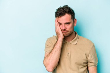 Mavi arka planda izole edilmiş, üzgün ve dalgın hisseden, kopyalama alanına bakan genç beyaz bir adam..