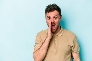 Mavi arka planda izole edilmiş genç beyaz adam yüksek sesle bağırıyor, gözleri açık ve elleri gergin tutuyor..