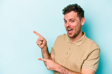 Mavi arka planda izole edilmiş genç beyaz adam işaret parmağıyla fotokopi alanını işaret ederek heyecan ve arzusunu ifade ediyor..