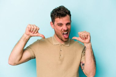 Mavi arka planda izole edilmiş genç beyaz adam gururlu ve kendinden emin hissediyor, örnek olarak.