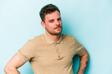 Kafkasyalı genç adam mavi arka planda izole edilmiş hoşnutsuzca kaşlarını çatmış, kollarını kavuşturmuş..